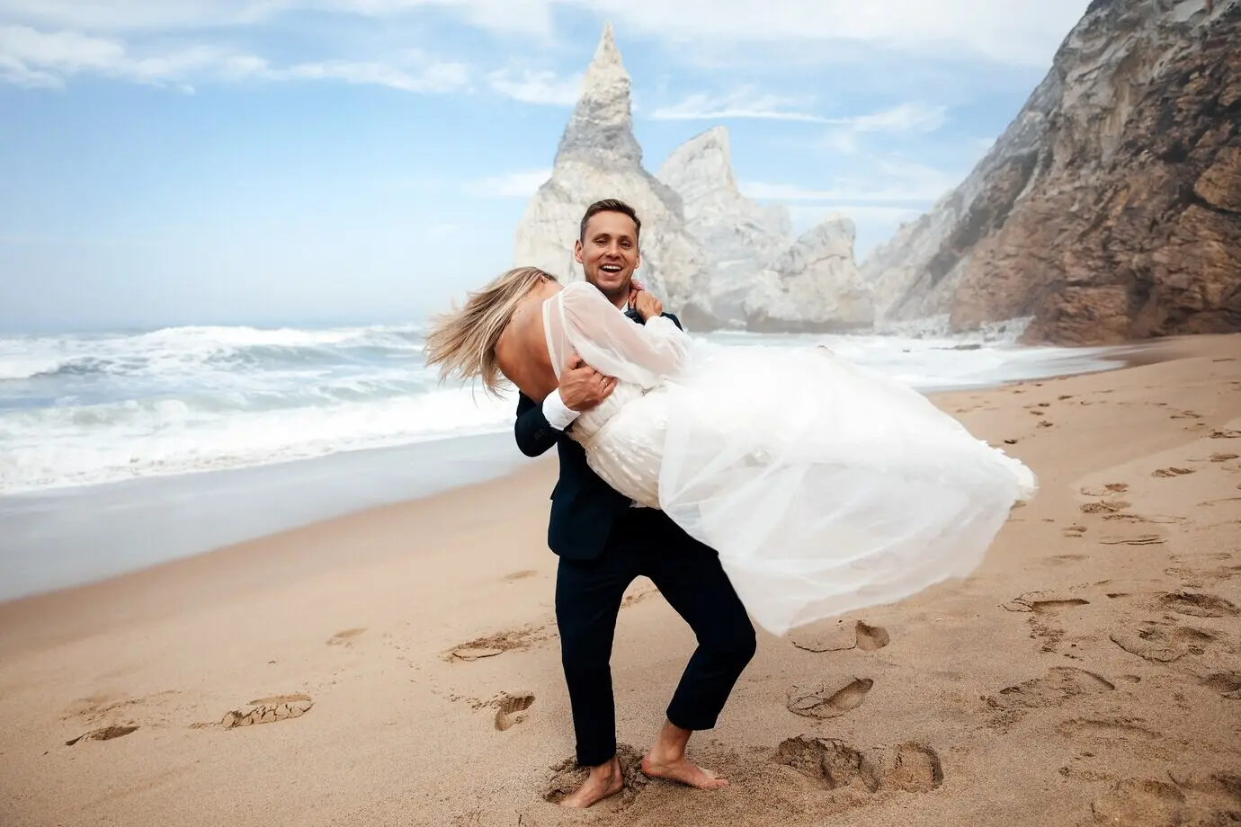 Мужчина держит свою жену на руках, и они выглядят очень счастливыми.